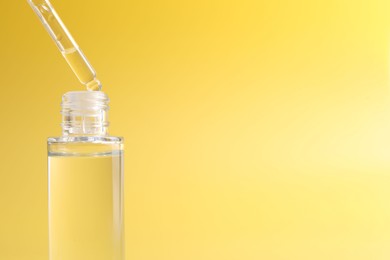 Photo of Dripping serum from pipette into bottle on yellow background, closeup. Space for text