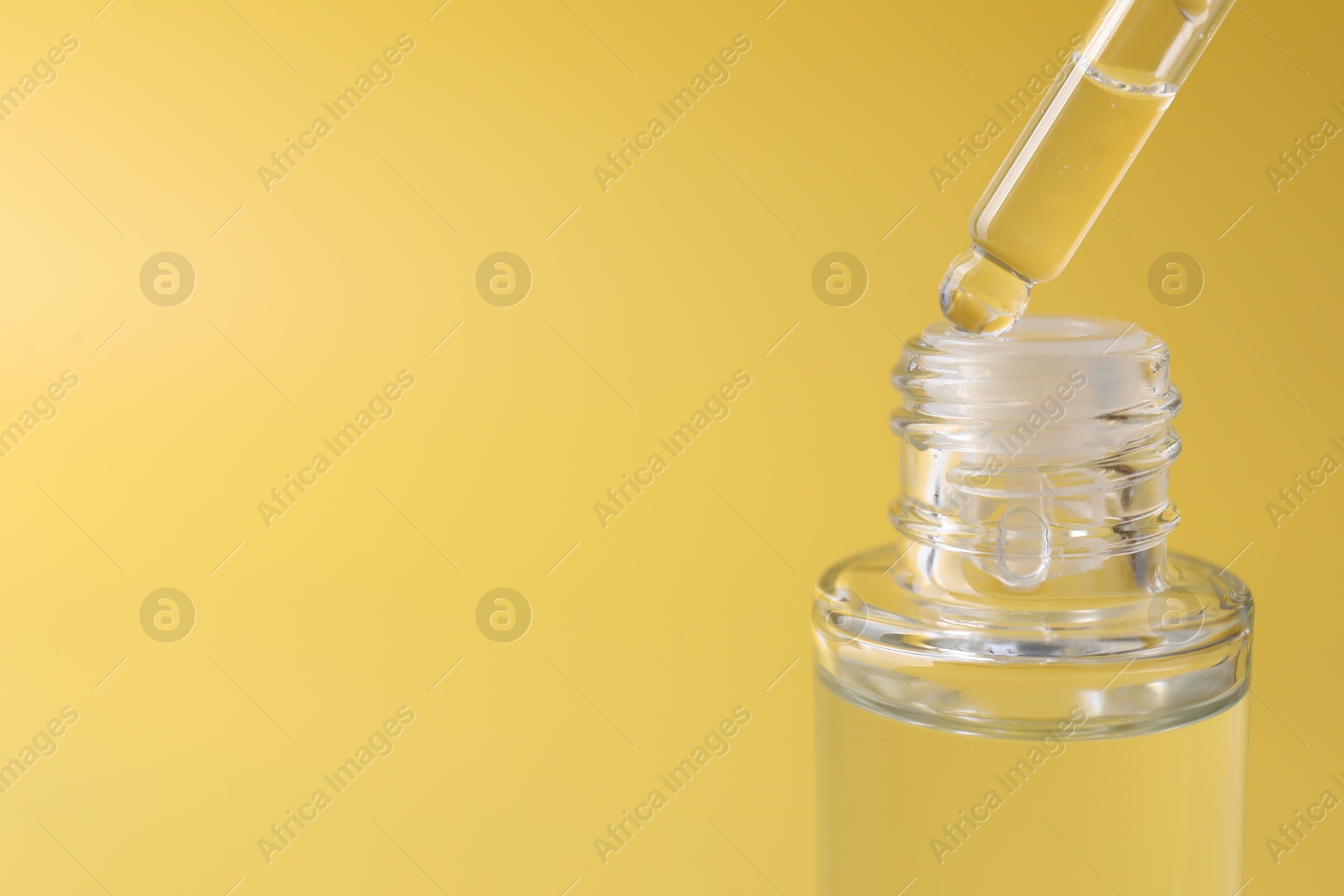 Photo of Dripping serum from pipette into bottle on yellow background, closeup. Space for text