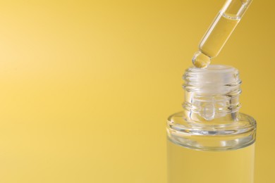 Photo of Dripping serum from pipette into bottle on yellow background, closeup. Space for text