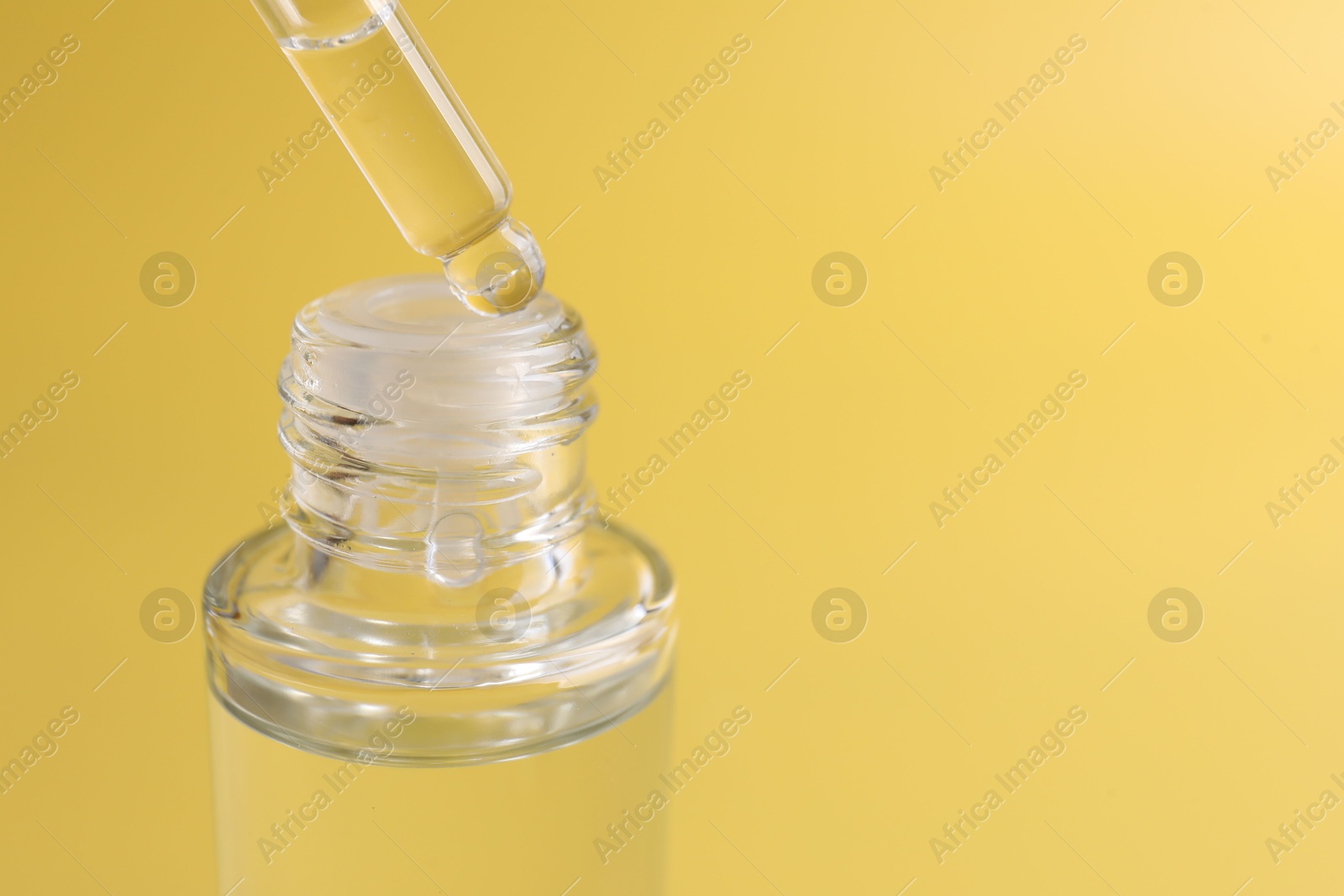 Photo of Dripping serum from pipette into bottle on yellow background, closeup. Space for text