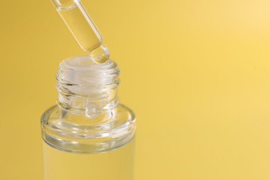 Dripping serum from pipette into bottle on yellow background, closeup. Space for text