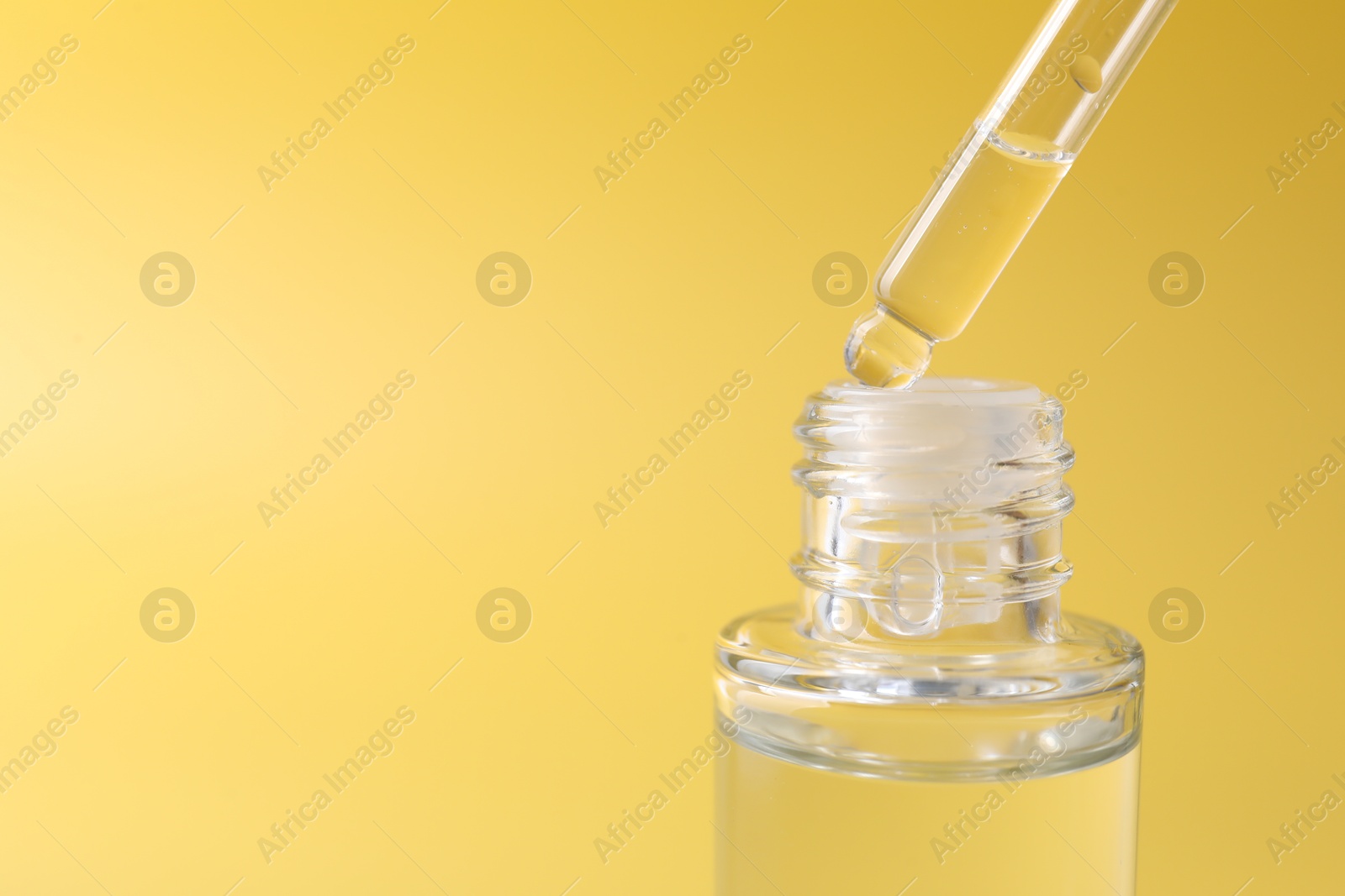 Photo of Dripping serum from pipette into bottle on yellow background, closeup. Space for text