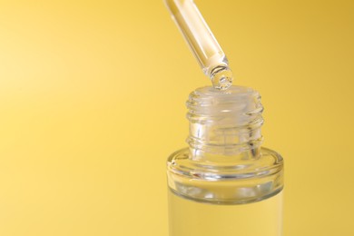 Dripping serum from pipette into bottle on yellow background, closeup. Space for text