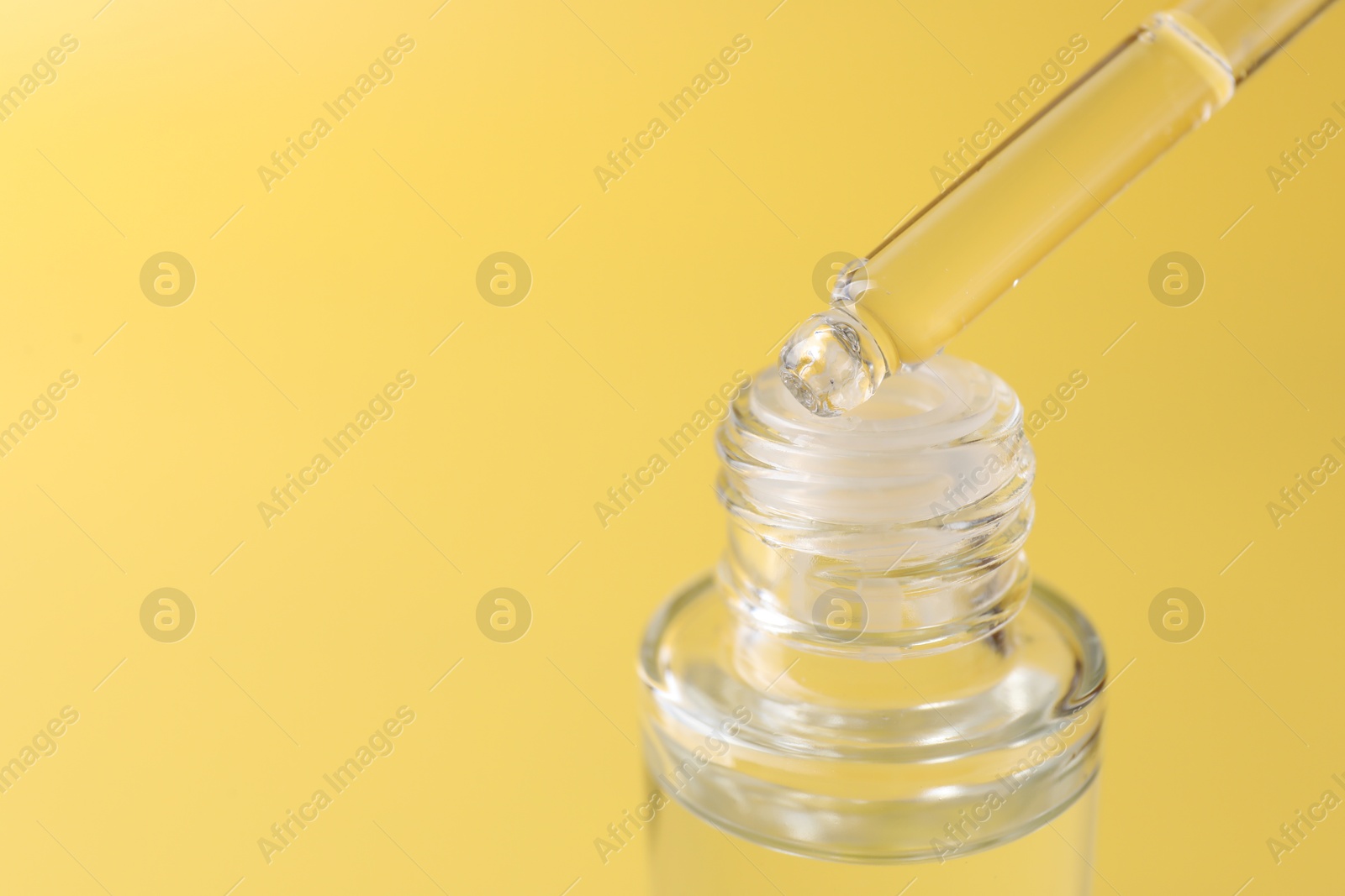 Photo of Dripping serum from pipette into bottle on yellow background, closeup. Space for text