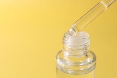 Dripping serum from pipette into bottle on yellow background, closeup. Space for text