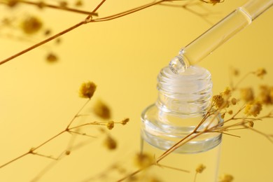 Dripping serum from pipette into bottle and gypsophila flowers on yellow background, closeup