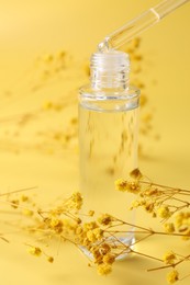 Photo of Dripping serum from pipette into bottle and gypsophila flowers on yellow background, closeup