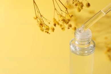 Dripping serum from pipette into bottle and gypsophila flowers on yellow background, closeup. Space for text