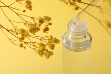 Dripping serum from pipette into bottle and gypsophila flowers on yellow background, closeup