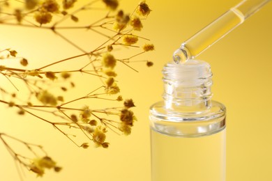 Dripping serum from pipette into bottle and gypsophila flowers on yellow background, closeup