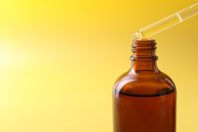 Dripping serum from pipette into bottle on yellow background, closeup. Space for text