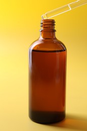 Dripping serum from pipette into bottle on yellow background, closeup