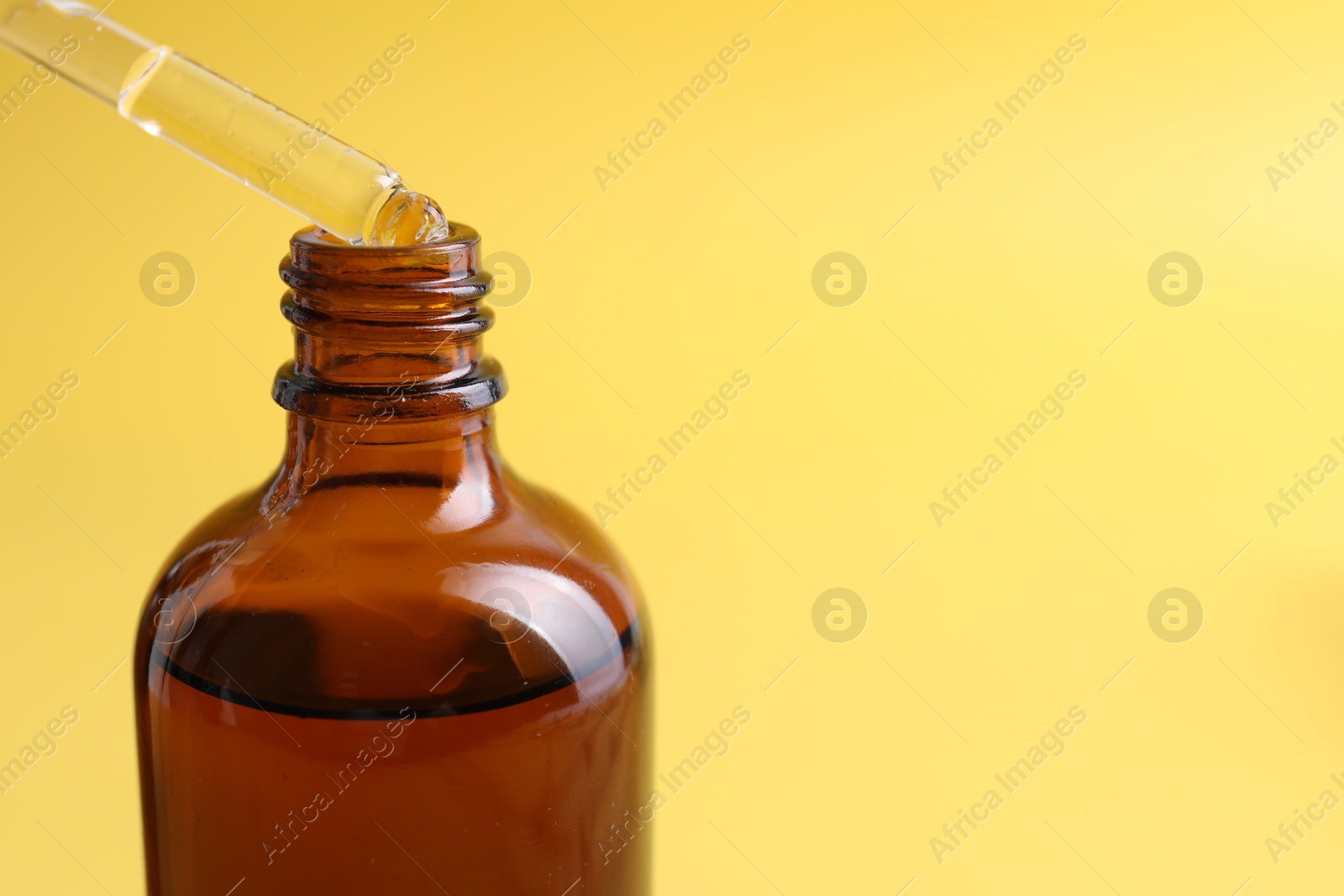 Photo of Dripping serum from pipette into bottle on yellow background, closeup. Space for text