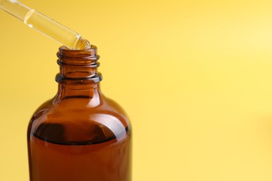 Dripping serum from pipette into bottle on yellow background, closeup. Space for text