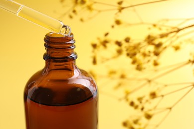 Dripping serum from pipette into bottle on yellow background, closeup. Space for text