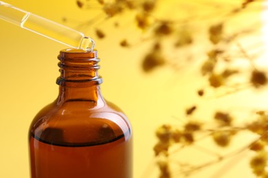 Photo of Dripping serum from pipette into bottle on yellow background, closeup. Space for text