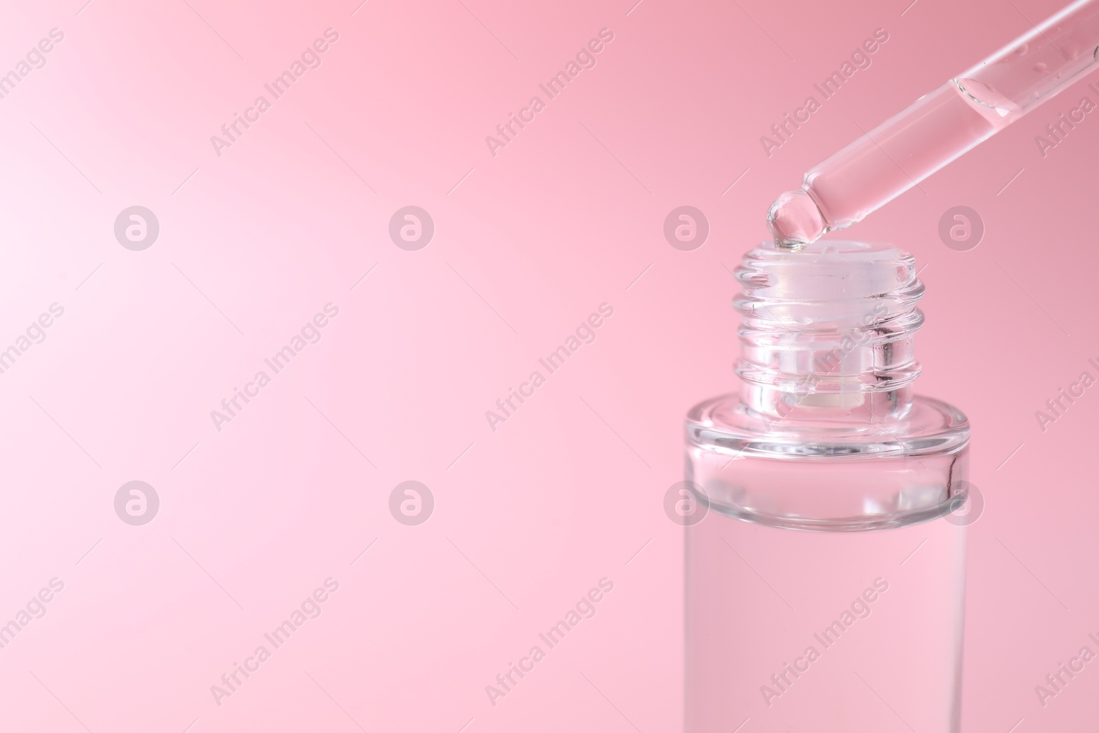 Photo of Dripping serum from pipette into bottle on pink background, closeup. Space for text