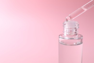 Photo of Dripping serum from pipette into bottle on pink background, closeup. Space for text