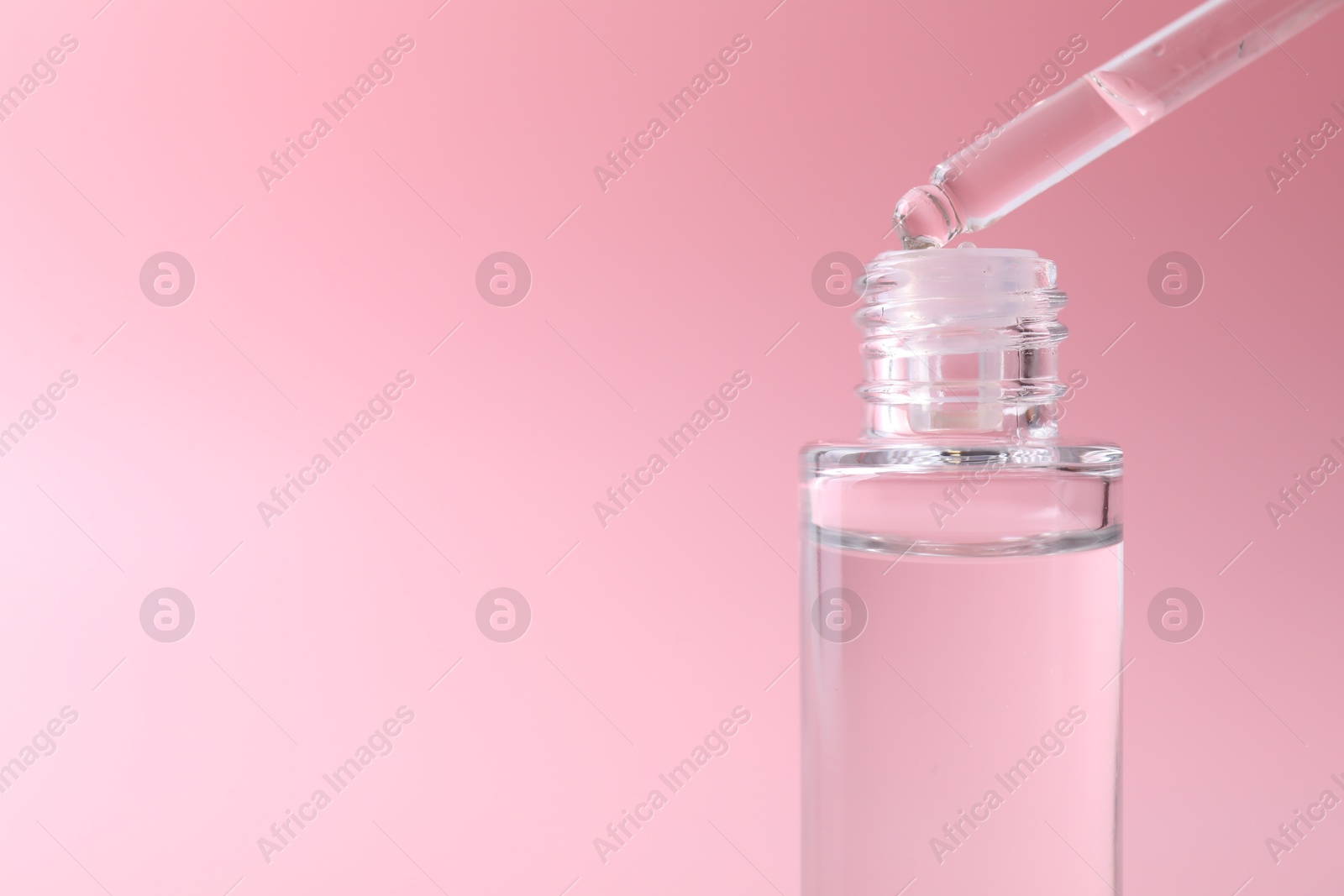 Photo of Dripping serum from pipette into bottle on pink background, closeup. Space for text