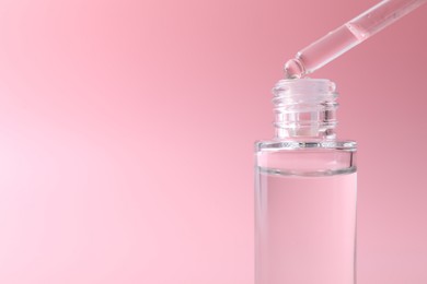 Dripping serum from pipette into bottle on pink background, closeup. Space for text