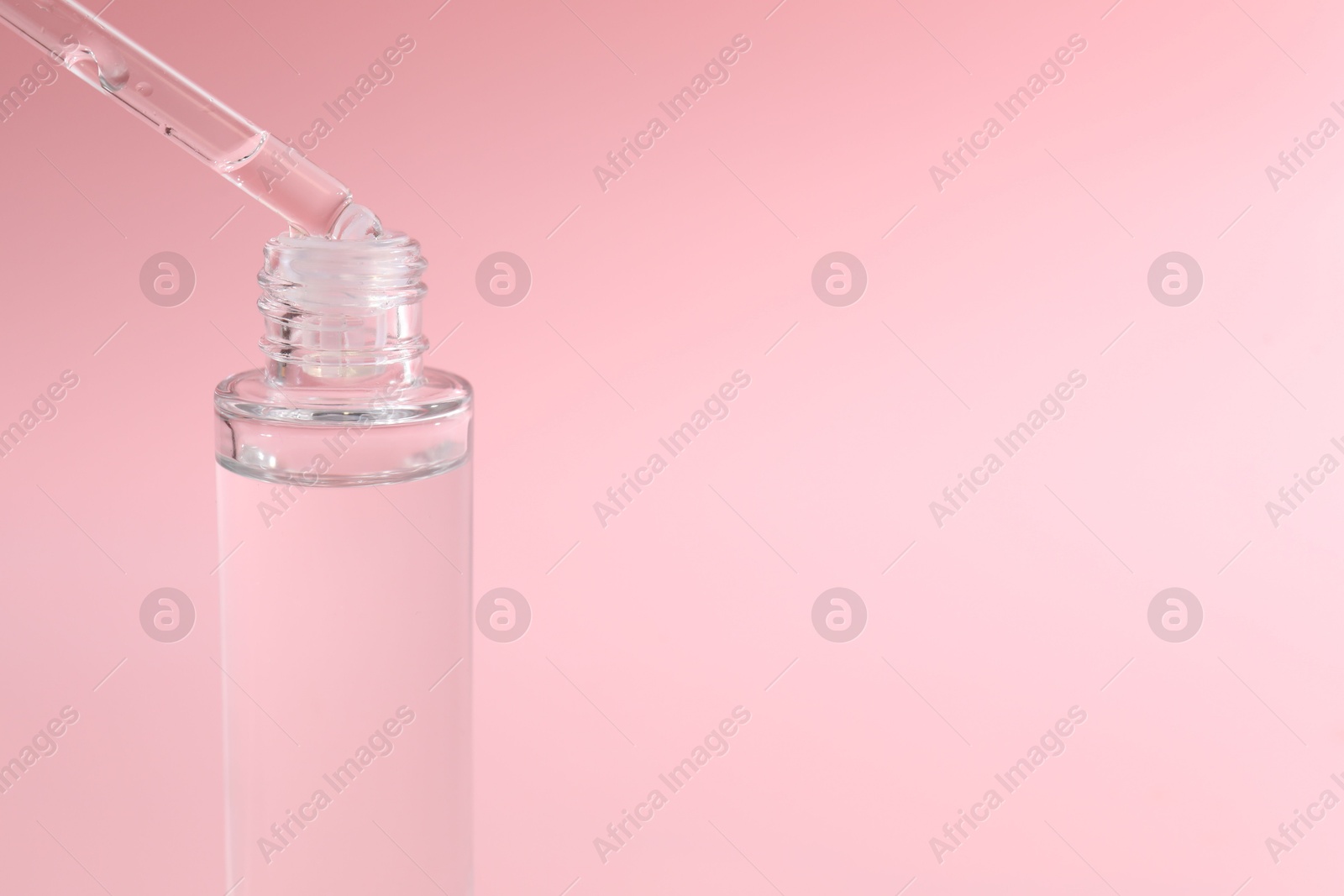 Photo of Dripping serum from pipette into bottle on pink background, closeup. Space for text