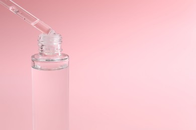 Photo of Dripping serum from pipette into bottle on pink background, closeup. Space for text