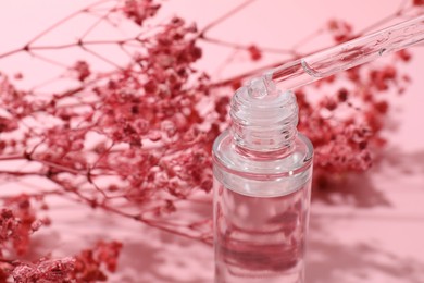 Dripping serum from pipette into bottle and gypsophila flowers on pink background, closeup