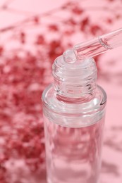 Photo of Dripping serum from pipette into bottle on blurred pink background, closeup