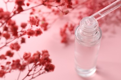 Dripping serum from pipette into bottle and gypsophila flowers on pink background, closeup