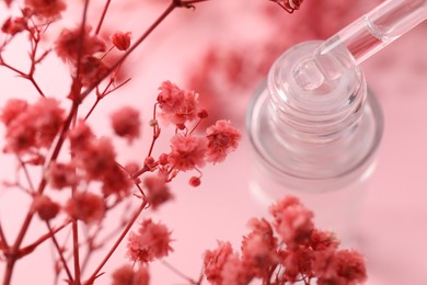 Photo of Dripping serum from pipette into bottle and gypsophila flowers on pink background, closeup