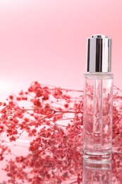 Photo of Bottle of serum and gypsophila flowers on mirror surface against pink background