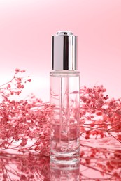 Photo of Bottle of serum and gypsophila flowers on mirror surface against pink background