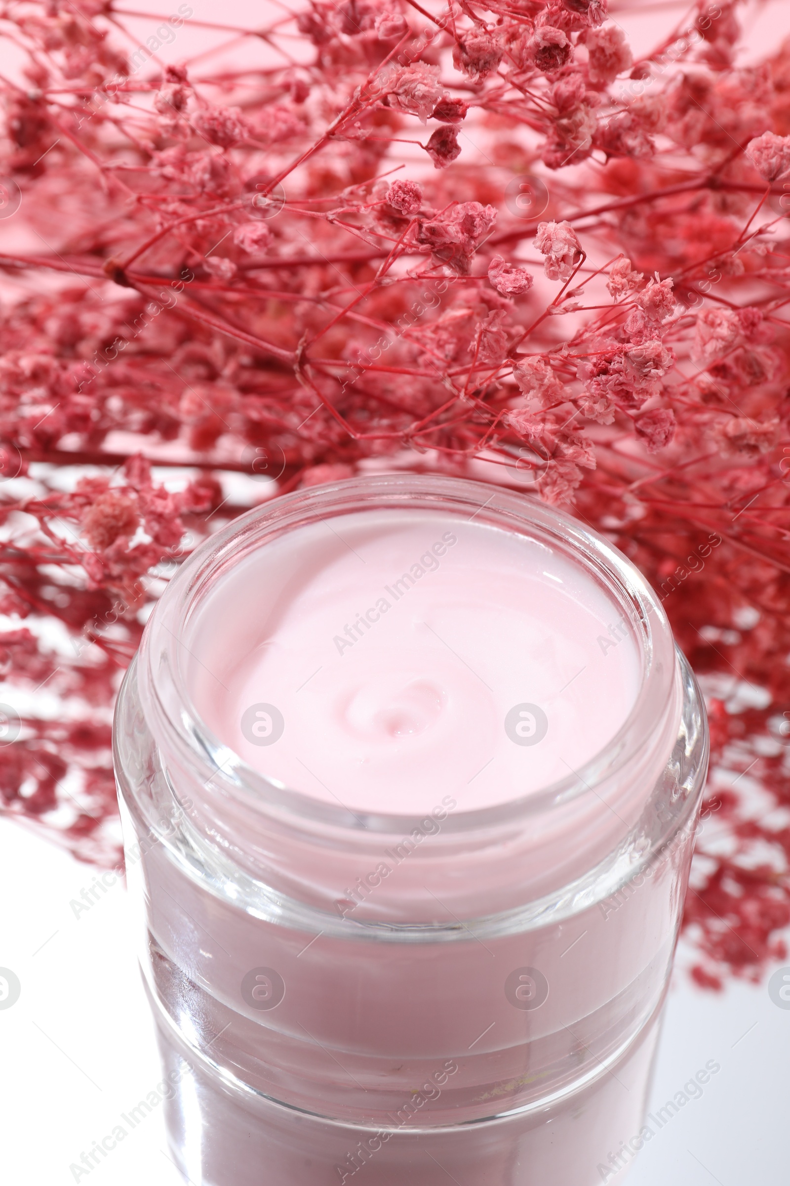 Photo of Jar of cream and gypsophila flowers on mirror surface, closeup