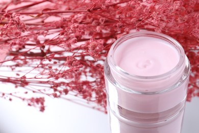 Jar of cream and gypsophila flowers on mirror surface, closeup