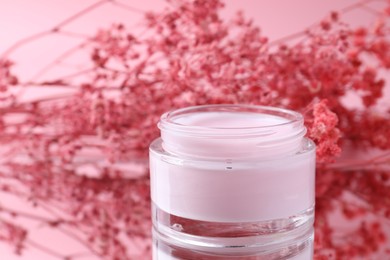 Photo of Jar of cream and gypsophila flowers on mirror surface against pink background, closeup