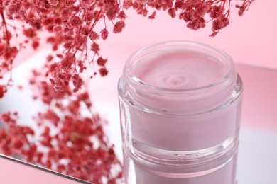 Photo of Jar of cream and gypsophila flowers on mirror surface against pink background, closeup