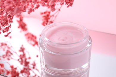 Photo of Jar of cream and gypsophila flowers on mirror surface against pink background, closeup