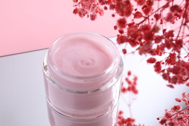 Photo of Jar of cream and gypsophila flowers on mirror surface against pink background, closeup