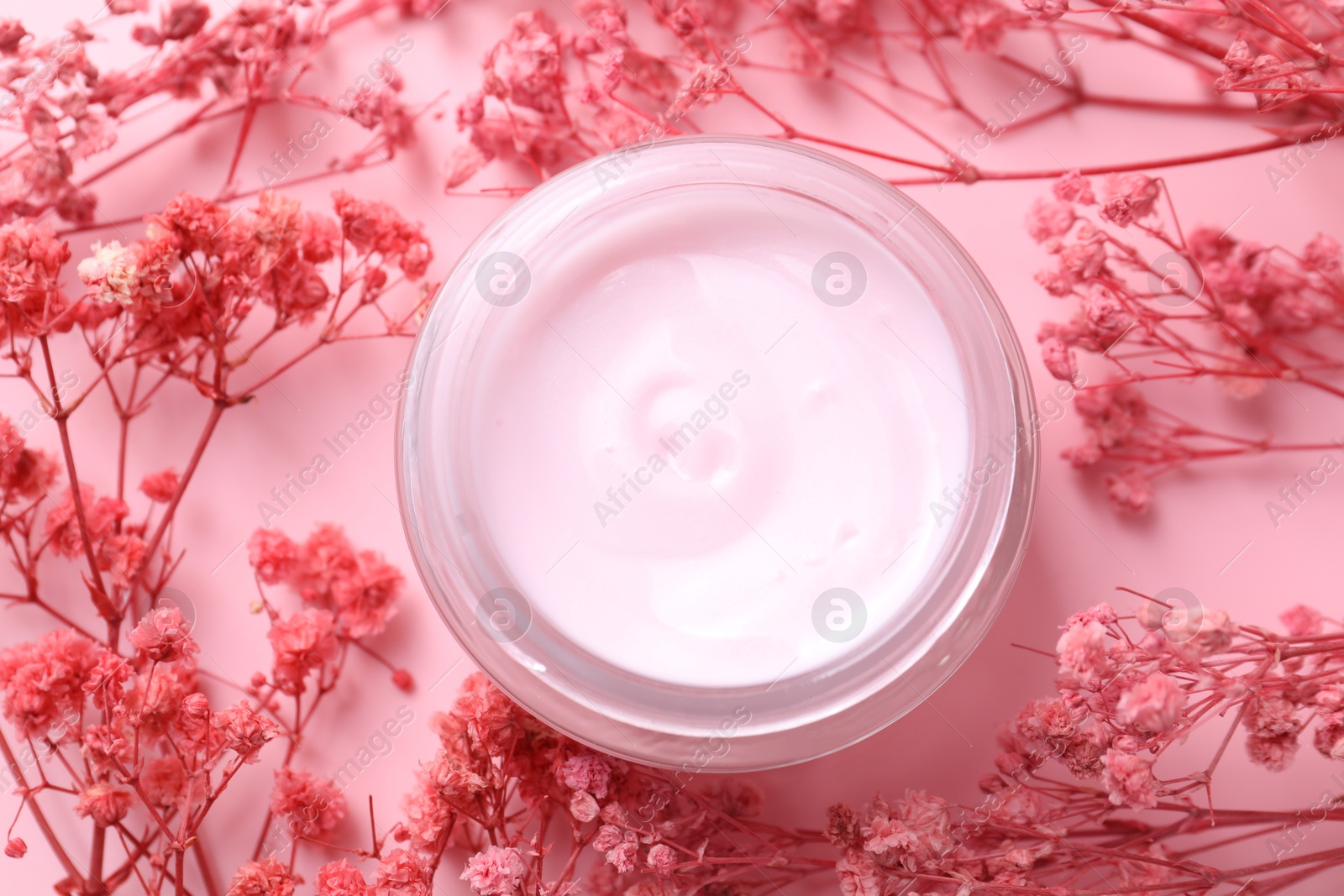 Photo of Jar of moisturizing cream among gypsophila flowers on pink background, flat lay