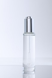 Photo of Bottle of serum on mirror surface against light background