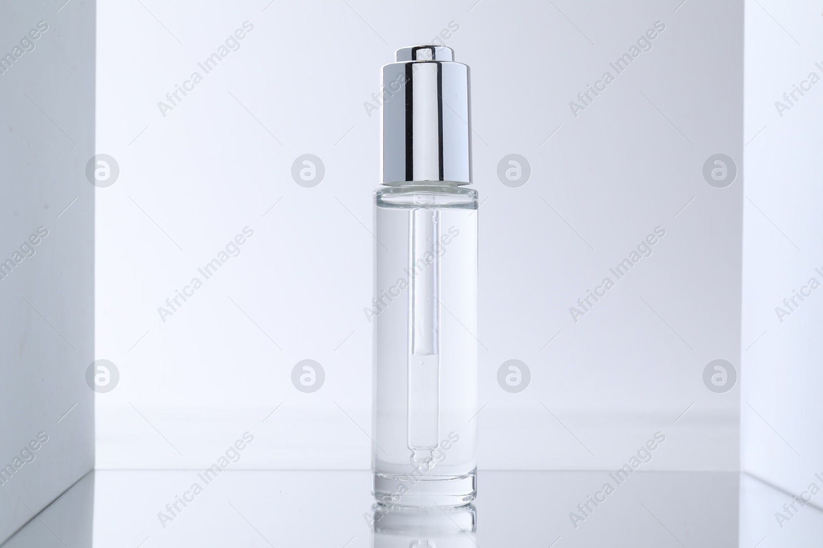 Photo of Bottle of serum on mirror surface against light background