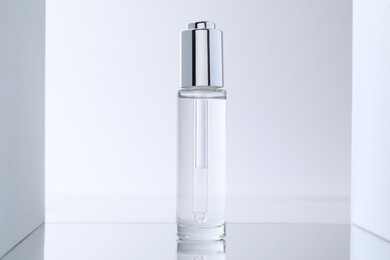 Photo of Bottle of serum on mirror surface against light background