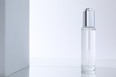 Photo of Bottle of serum on mirror surface against light background. Space for text