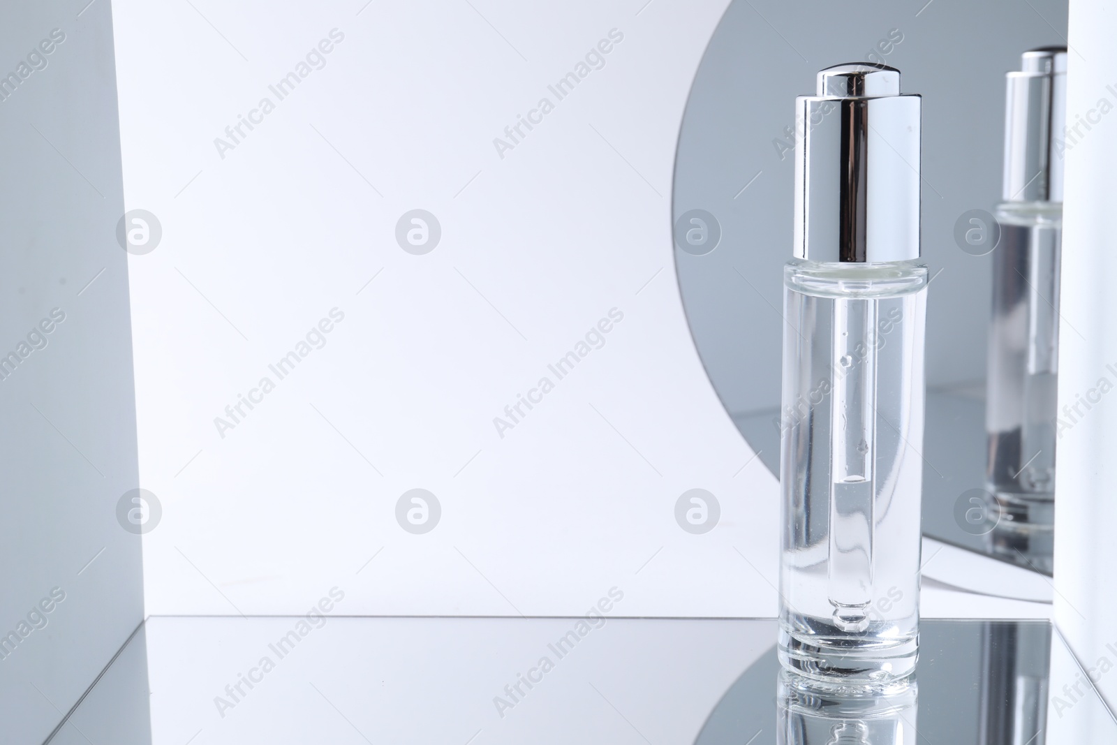 Photo of Bottle of serum on mirror surface against light background. Space for text