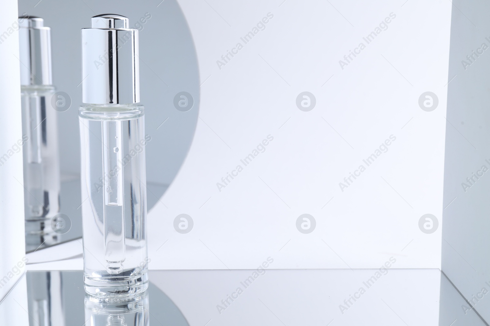 Photo of Bottle of serum on mirror surface against light background. Space for text