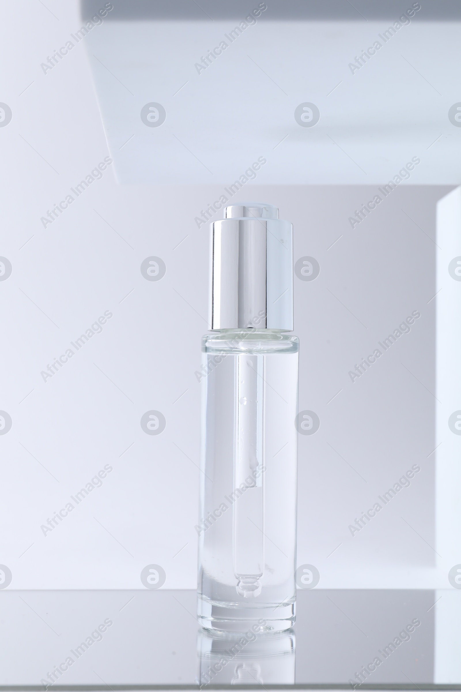 Photo of Bottle of serum on mirror surface against light background