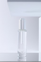 Bottle of serum on mirror surface against light background