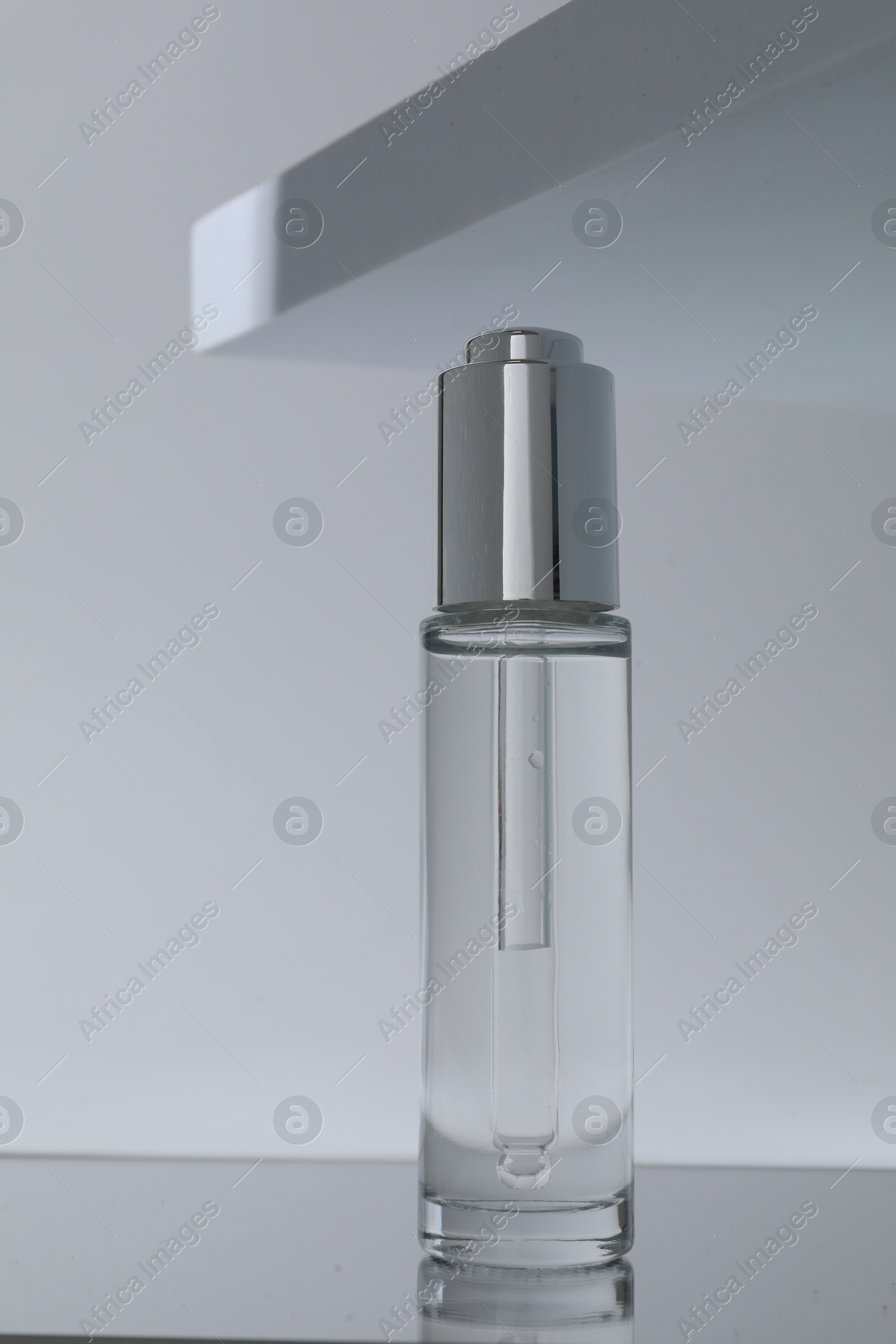 Photo of Bottle of serum on mirror surface against grey background, closeup