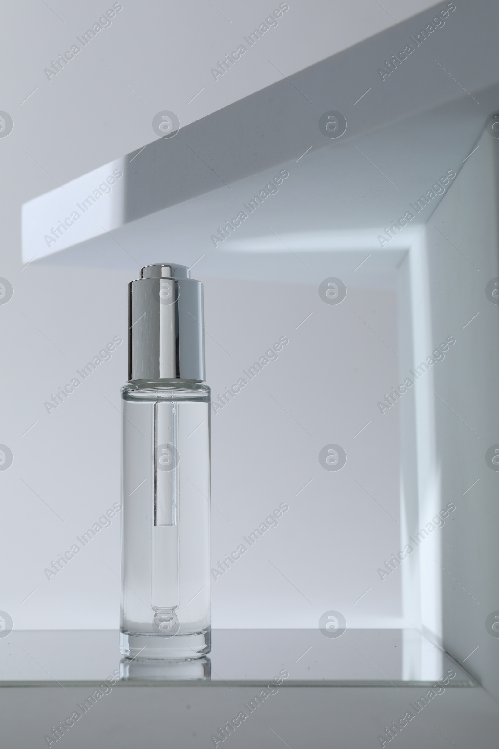 Photo of Bottle of serum on mirror surface against grey background