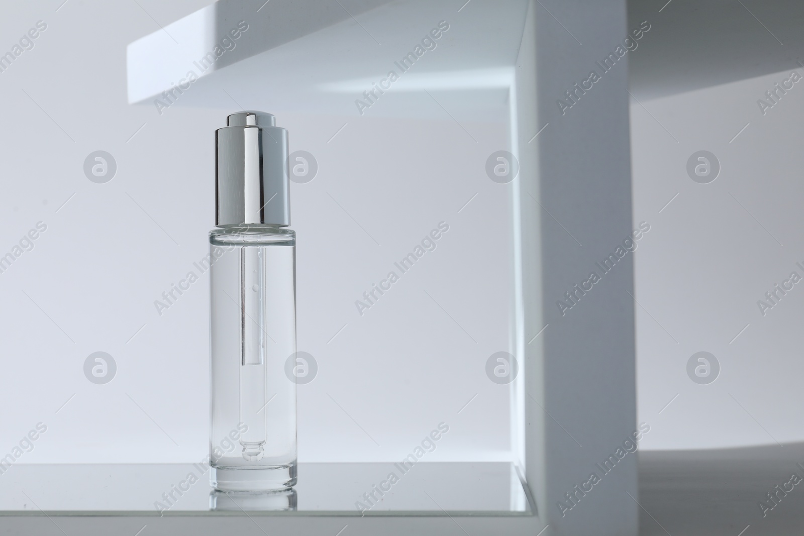 Photo of Bottle of serum on mirror surface against light background